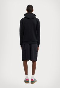 Sudadera con capucha negra, pantalones cortos cargo oscuros con bolsillos y zapatillas de deporte coloridas. Tejido suave y corte relajado. Diseño simple sin patrones.