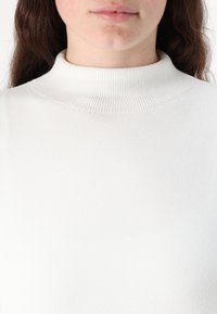 White ribbed turtleneck sweater with a smooth texture and fitted design, emphasizing the high neck and soft material.
