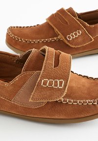 Brune ruskindsko med en velcrorem, dekorativ syning, teksturerede detaljer og en fleksibel gummiydersåle.