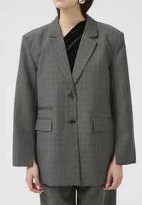 Grauer karierten Blazer mit lockerer Passform, zwei vorderen Taschen und einem Ein-Knopf-Verschluss. Verfügt über breite Revers und seitliche Belüftung.