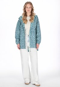 Chaqueta con estampado de leopardo en color azul verdoso, con capucha, puños elásticos y cremallera frontal. Combinada con vaqueros de pierna ancha de color claro y zapatillas deportivas.