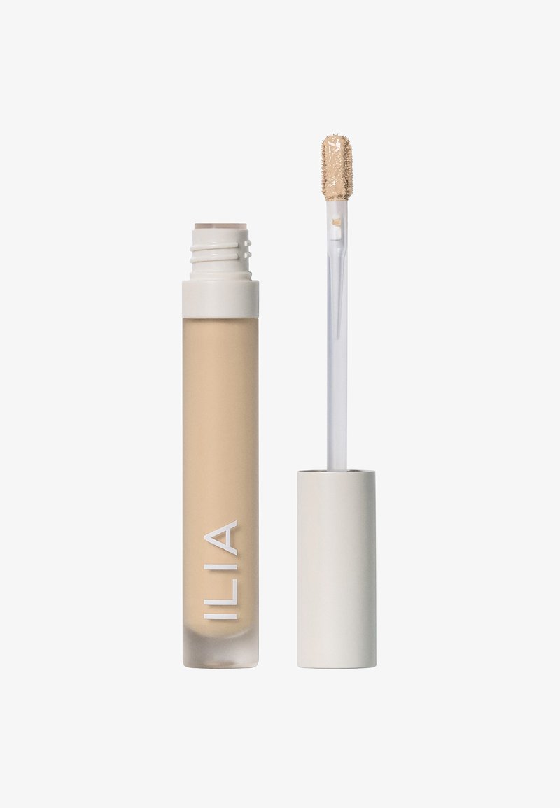 ILIA concealer i en genomskinlig tub med beiget innehåll synligt. Har ett vitt lock och en klar applikator med en texturerad topp.