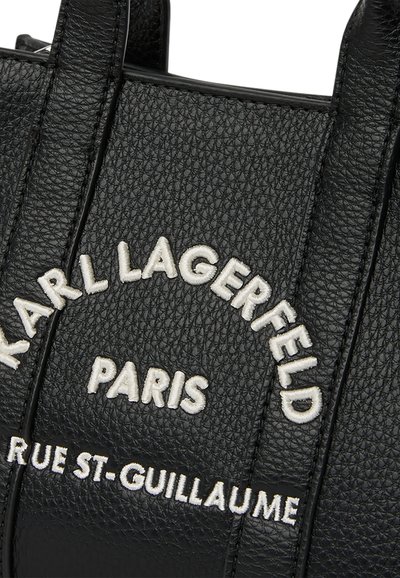 Черен текстуриран кожен чант с бял бродиран текст с надпис "KARL LAGERFELD PARIS RUE ST-GUILLAUME" на предната част.