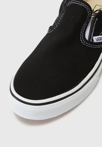 Fekete vászon slip-on cipő kerek orral, fehér gumitalppal és kontrasztos fehér varrással, valamint szegéllyel a szélein.