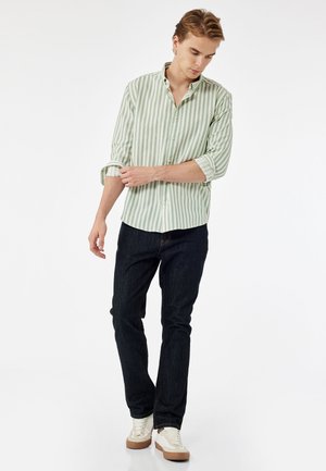 Camisa de manga larga de rayas verdes claras y blancas con cuello abotonado. Combinada con jeans de mezclilla oscura y zapatillas blancas.