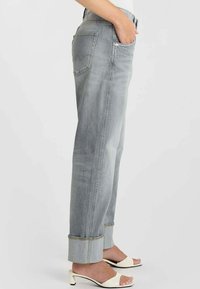 Grijze denimjeans met een losse pasvorm, voorzien van opgerolde pijpen, achterzakken en contrasterende stiknaden. Gecombineerd met witte open-toe hakken.