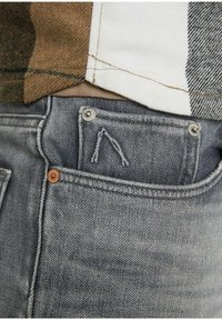 Grå denimjeans har en texturerad yta med en urtvättad finish. Framsidan har en liten sydd detalj och två metallknappar.