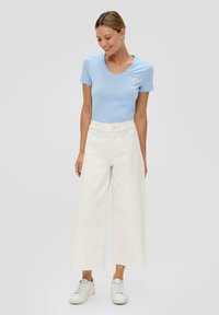 Helles blaues T-Shirt mit kurzen Ärmeln und floraler Stickerei, kombiniert mit hoch taillierten, weit geschnittenen weißen Jeans und weißen Sneakern.