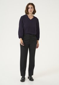 Navy blouse with a V-neck and ruffled collar, paired with black tailored trousers and black lace-up shoes, on a plain background.