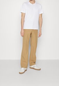 White cotton t-shirt with short sleeves, paired with light brown tailored pants and white sneakers featuring beige accents.