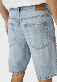 Șorturi din denim de culoare albastru deschis, cu o croială lejeră, având buzunare pe spate, margine descusută și o etichetă din piele maro cu numele brandului la talie.