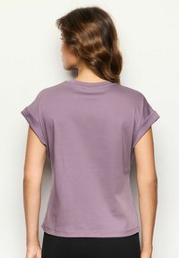 T-shirt a maniche corte di colore lavanda con maniche arrotolate, scollatura rotonda, tessuto morbido e vestibilità rilassata, vista da dietro.
