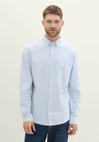 Camisa de botones de color azul claro con rayas verticales blancas, que cuenta con un bolsillo en el pecho y mangas largas. Fabricada con un tejido suave y liso.