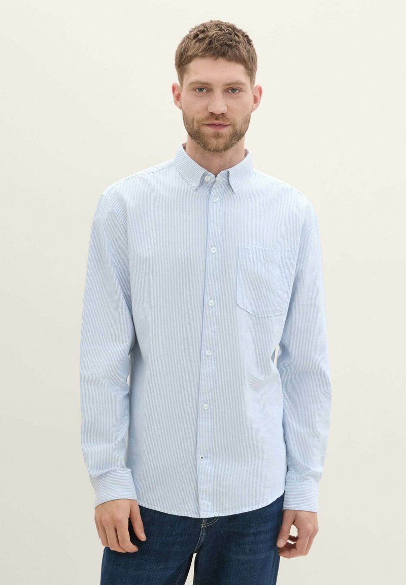 Camisa de botones de color azul claro con rayas verticales blancas, que cuenta con un bolsillo en el pecho y mangas largas. Fabricada con un tejido suave y liso.