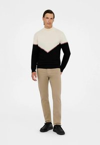 Svart och krämfärgad stickad tröja med ett V-format mönster och röda accentinjer. Bärs med beige byxor och svart skor.