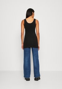 Top sin mangas negro con escote redondeado, combinado con jeans azules de pierna ancha, que exhibe una textura suave y un ajuste casual.