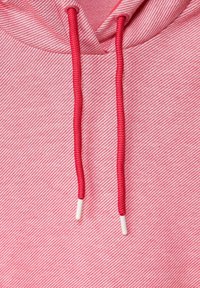 Nærbillede af pink og hvid stribet hættetrøje-stof med to røde snore, der ender i hvide plastikspidser.