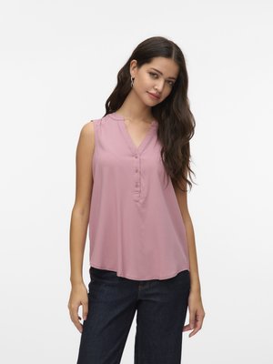 Sleeveless pink blouse with buttoned placket, v-neckline, and relaxed fit. Soft fabric with slight sheen; model paired with dark denim.