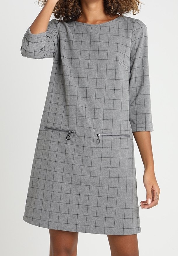 Vestido gris con un patrón de cuadros, mangas tres cuartos, dos bolsillos con cremallera y un escote redondo. Tejido suave con una textura lisa.