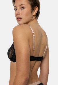 Soutien-gorge en dentelle noire avec un motif floral délicat, des bretelles en satin doux et une fermeture à crochets, présentant un design moderne et complexe.