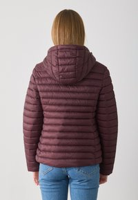 Bordo jakna s kapuljačom, kvadratičnog izgleda, s horizontalnim šavovima, prilagođenog kroja i mekog, pahuljastog materijala. Nosena preko plavih traperica.
