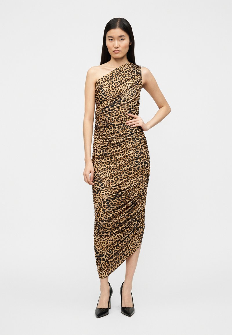 Robe imprimé léopard, design asymétrique à une épaule, texture froncée, longueur genoux, en nuances de brun et noir, associée à des escarpins noirs.