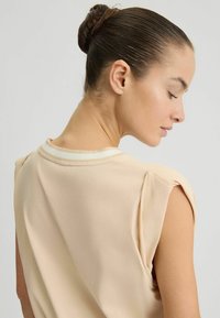 Top beige senza maniche con scollatura rotonda, caratterizzato da un bordo a righe in contrasto. Tessuto morbido con una consistenza liscia, visto dalla schiena.