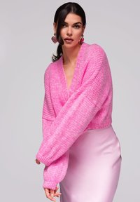 Růžový pletený svetr s hlubokým V výstřihem a oversize rukávy, kombinovaný s elegantní růžovou saténovou sukní. Texturovaný, měkký materiál.