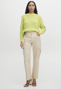 Hellegrüner gestrickter Pullover mit lockerer Passform und Ripptextur, kombiniert mit beigen Cargo-Hosen mit seitlichen Taschen und gerader Beinform.