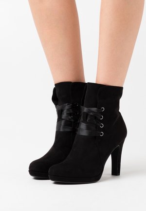 Bottines en suède noir avec un talon haut, dotées d'un design lacé avec un ruban en satin et des œillets en métal, texture lisse.