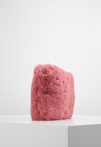 Pochette rose en fausse fourrure avec une surface texturée, de forme rectangulaire, et une petite boucle en métal argenté sur un côté.