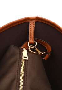 Wnętrze torby wykonanej z płótna z brązowymi skórzanymi wykończeniami, z czarną podszewką, złotym zamkiem błyskawicznym, zapięciem na haczyk oraz gładkimi detalami.