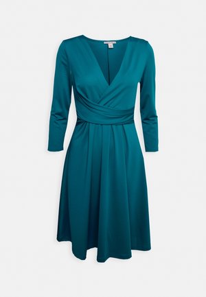 Blauwgroene jurk tot op de knie met lange mouwen, V-hals en geplooide taille, weergegeven op een witte achtergrond.