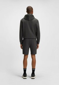 Tuta sportiva grigia con felpa con cappuccio e pantaloni corti coordinati. Materiale liscio, design aderente e lunghezza corta per una maggiore mobilità.