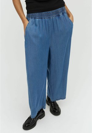 Denim wide-leg pants in light blue with an elastic waistband, side pockets, and contrasting stitching details. Paired with black shoes.