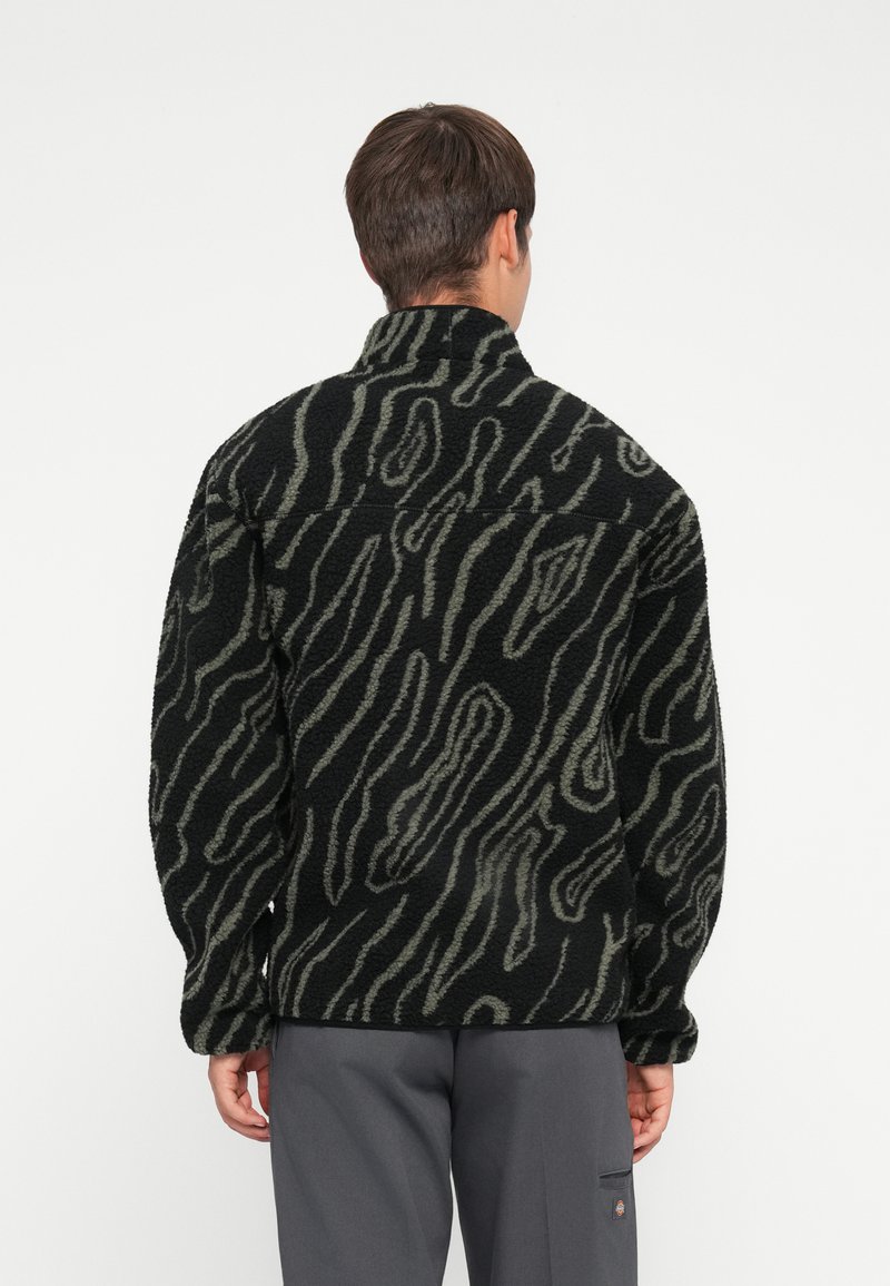 Sorte og olivengrøn mønstrede fleecejakke med høj krave og oversized pasform, der har bølgede linjer og en tekstureret overflade.