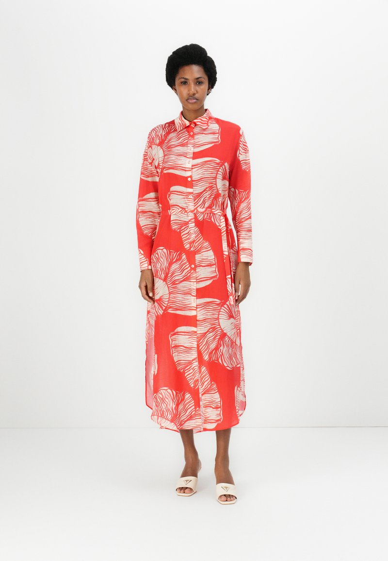 Rochie roșie cu mâneci lungi, cu un model floral alb, butoane pe toată lungimea din față și o siluetă fluidă. Stilizată cu sandale neutre, ușor de purtat.