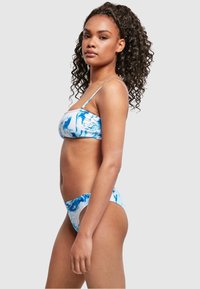 Bikini set uzorka plave i bijele mramorne boje s bandeau topom i tankim trakama te s niskim gaćicama, izrađen od rastezljivog materijala za kupanje.