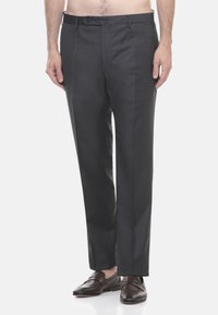 Uomo che indossa pantaloni formali grigio scuro e mocassini in pelle marrone scuro, in piedi davanti a uno sfondo bianco semplice.