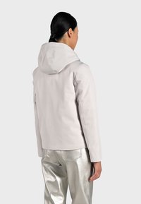 Jasnoszara wodoodporna kurtka z kapturem, o dopasowanym kroju i gładkiej fakturze, zestawiona z błyszczącymi srebrnymi spodniami.