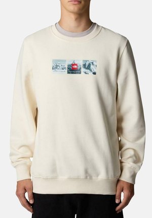 Sudadera de color crema claro con cuello redondo, que presenta tres imágenes de montañas impresas y un logo rojo en el centro. Tela texturizada, ajuste relajado.