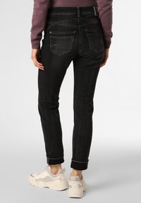 Vaqueros de mezclilla negros con un diseño ajustado, estilo de cinco bolsillos y puños remangados. Llevados con zapatillas de color claro con una parte superior texturizada.