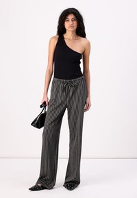 Top noir à une épaule avec des côtes, associé à un pantalon large rayé gris et des ballerines noires à bout pointu. Le mannequin tient un sac à main noir.