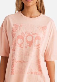 Lyserød bomulds t-shirt med oversized pasform, der har et grafisk print af tre cirkler og blomsterelementer, teksten lyder "Kissed by Moonlight."