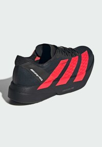 Sort atletisk sko med lyse røde skrå striber, struktureret overdel og polstret sål mærket "LIGHTSTRIKE PRO." Har et elegant design.