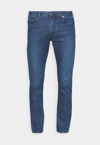 Blugi din denim albastru, cu o croială ajustată, cinci buzunare și clapă cu nasture. Materialul are o textură subtilă și accente ușor decolorate.