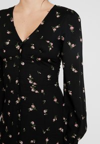 Sort kjole med V-hals, blomsterprint i pink og grøn, lange pufærmer og knapdetalje ned foran. Blødt stof.