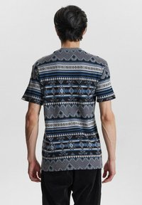 Camisa de manga corta en gris con patrones geométricos en azul y negro, con una textura suave y un corte regular.