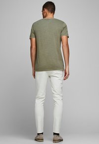 Olivenfarvet t-shirt med korte ærmer, tætsiddende pasform, parret med hvide tætsiddende bukser. Let stof med en blød tekstur. Casual fodtøj synligt.