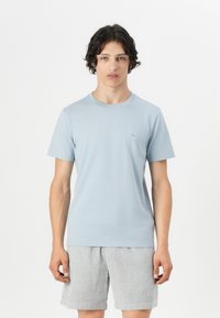 T-shirt en coton bleu clair avec un col rond, des manches courtes et un petit logo brodé sur la poitrine. Assorti à un short à rayures.